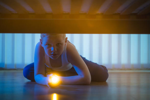 istock The boy with a flashlight look under bed. night time 1081139578