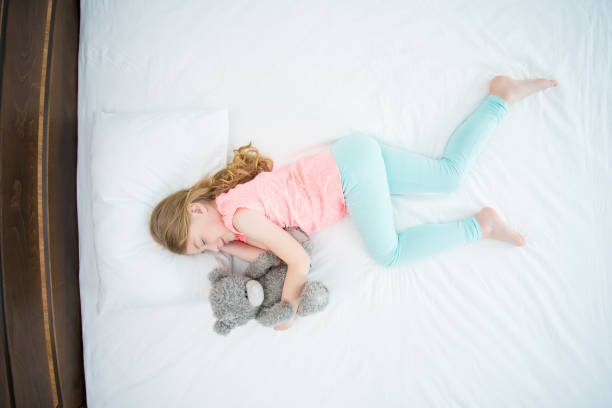 девушка с мягкой игрушкой спит на кровати. вид сверху - crane shot стоковые фото и изображения