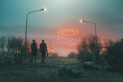 Couple walking towards flying UFOs.