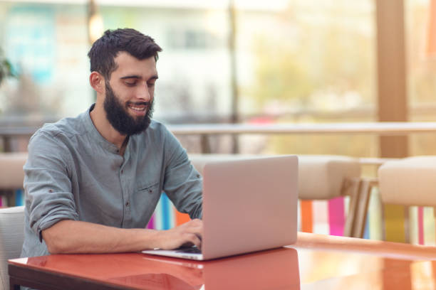 istock Half length portrait of successful bearded designer smiling at camera while working on freelance at netbook. 1081172532