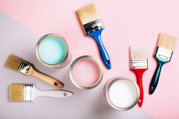 istock Three open cans of pastel paint with five brushes on pink and grey background. 1081176496