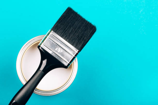 istock Brush with black handle on open can of white paint on blue background. 1081176520