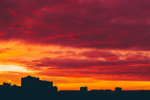istock Cityscape with vivid surrealistic dawn. Amazing warm dramatic cloudy sky above dark silhouettes of city buildings. Orange sunlight. Atmospheric background of sunrise in overcast weather. Copy space. 1081178048