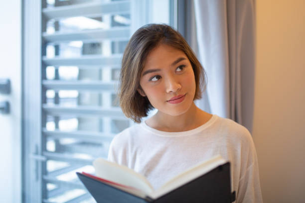 istock Content young woman reading book at window at home 1081190874