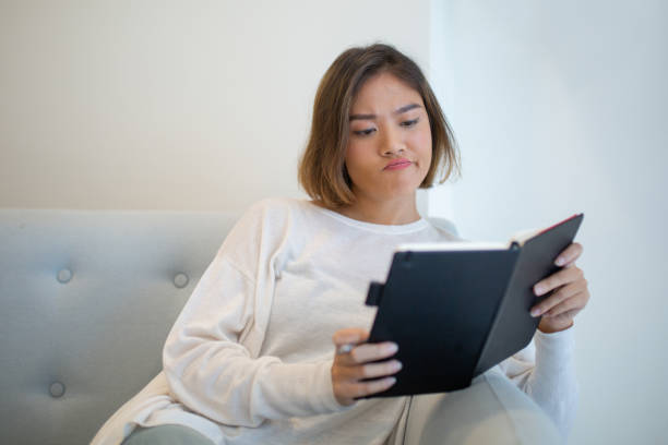 istock Skeptical young woman reading book on sofa at home 1081190942