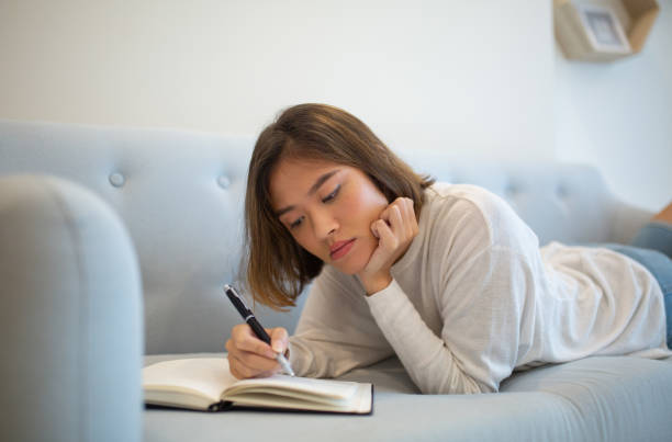 istock Serious woman making notes in notebook and lying on sofa at home 1081190950