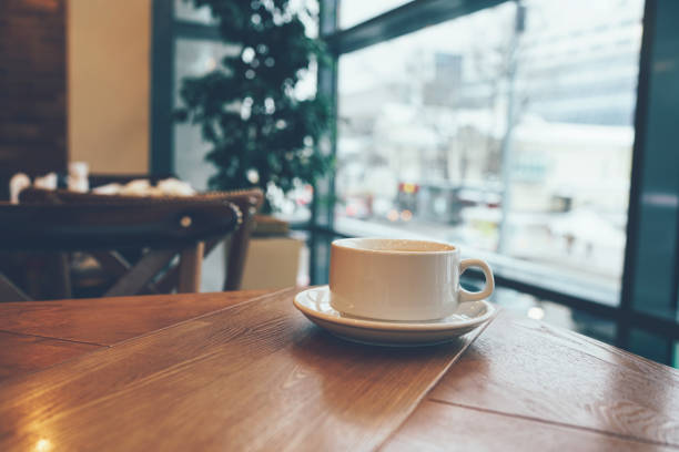 White Ñ"u0081up of coffee on the table by the window in modern cafe, White Ñ"u0081up of coffee on the table by the window in modern cafe, copy space ñu stock pictures, royalty-free photos & images