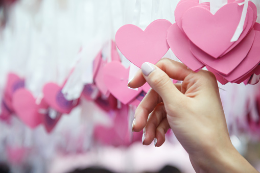 Woman Hand pick pink heart shape Lucky Draw attached to white ribbon on wishing tree in charity event. Games, that prizes are covered up and mixed up with other numbers, to raise money for charity.