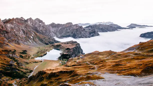 Aerial view over cloud, high grass land rocky alpine mountain valley and lake Trubsee of Titlis in Engelberg, Switzerland