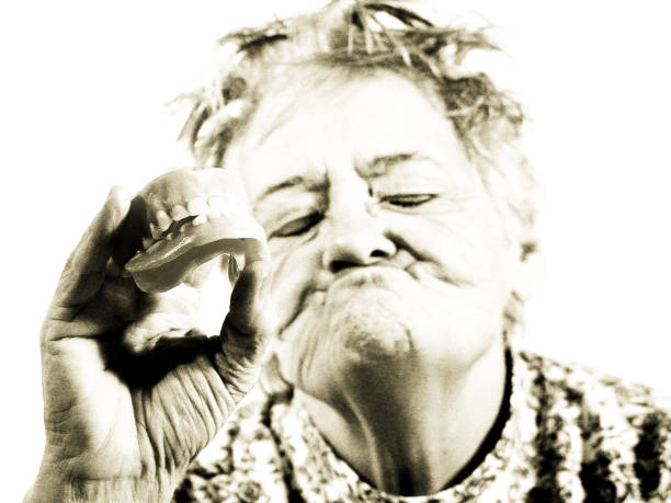 Senior woman showing off her false dentures. Closed eyes, toothless expression. 