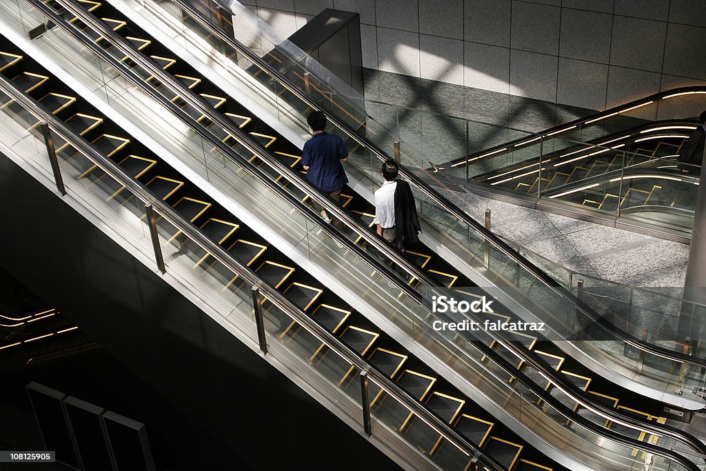 Dos personas Riding escalera mecánica en el edificio - Foto de stock de Escalera mecánica libre de derechos