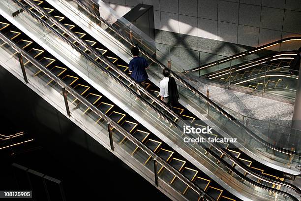 Dos Personas Riding Escalera Mecánica En El Edificio Foto de stock y más banco de imágenes de Escalera mecánica