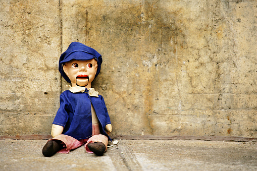 Ventriloquist Dummy Sitting Against Concrete Wall