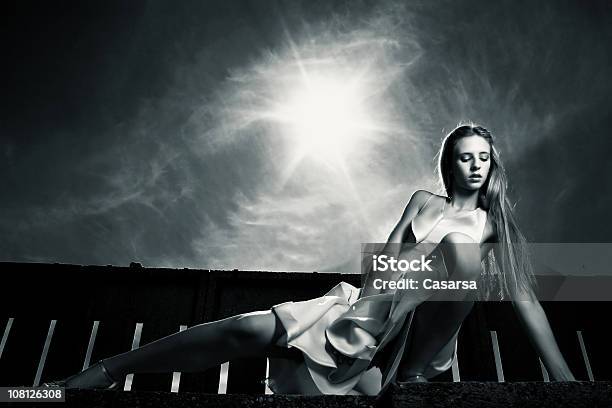 Young Woman Posing Near Fence With Dramatic Sky Toned Stock Photo - Download Image Now