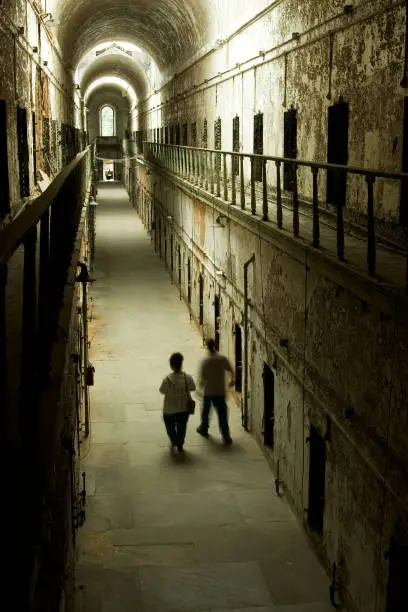 Photo of Two People Walking Through Old Abandoned Prison Hallway