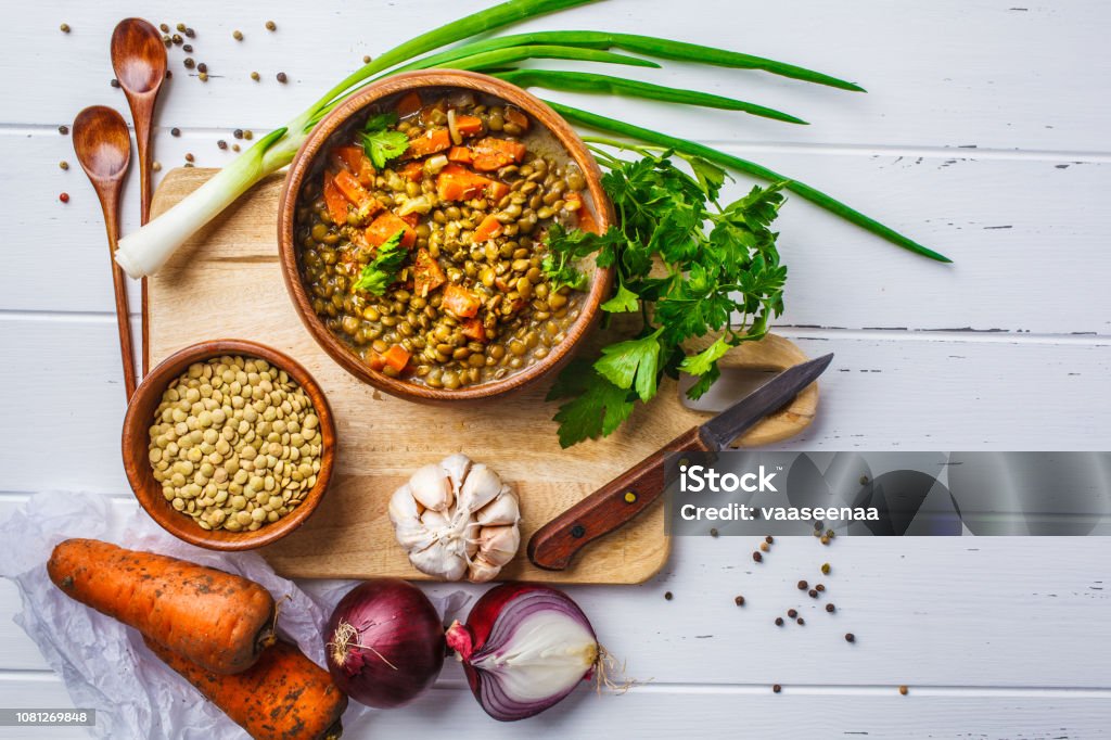 Lentil soup in a wooden bowl and ingredients on a white wooden background, top view. Lentil vegan soup in a wooden bowl and ingredients on a white wooden background, top view. Lentil Stock Photo