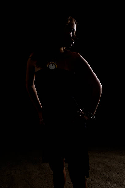 Studio shot of full length brunette woman in a sleeveless black dress posing dramatically with hand on forehead on white background