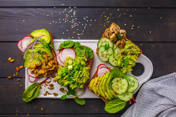 Photo of Avocado toasts with different toppings, top view, dark wooden background.