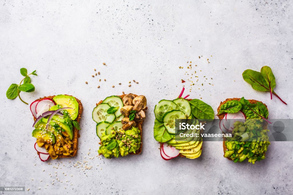 Avocado toasts with different toppings, top view, white background, copy space. Avocado toasts with different toppings, top view, white background. Plant based diet concept. Avocado Stock Photo