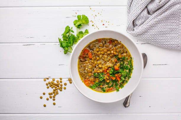 Homemade vegan lentil soup with vegetables and cilantro, white wooden background. stock photo