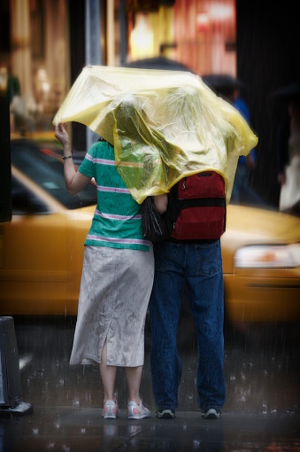 A couple wait to cross the street while rain pours down over them.