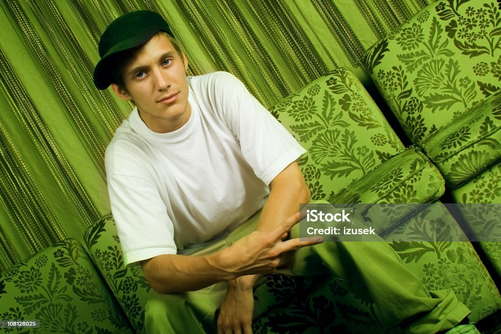 Jeune homme assis sur un canapé avec Attitude - Photo de Signe de la paix libre de droits