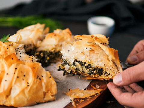Slice of greek pie spanakopita in hand. Ideas and recipes for vegetarian or vegan Spanakopita Spinach Pie from fillo pastry cut in slices. Copy space. Side view
