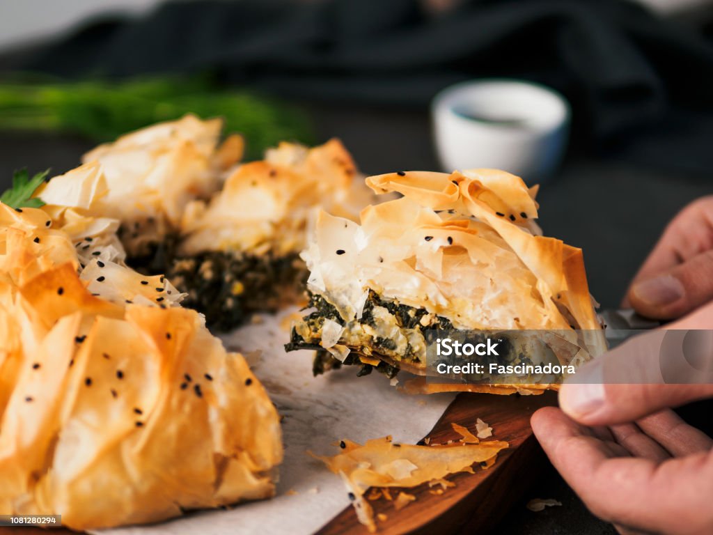 Vegan Spanakopita Spinach Pie Slice of greek pie spanakopita in hand. Ideas and recipes for vegetarian or vegan Spanakopita Spinach Pie from fillo pastry cut in slices. Copy space. Side view Savory Pie Stock Photo
