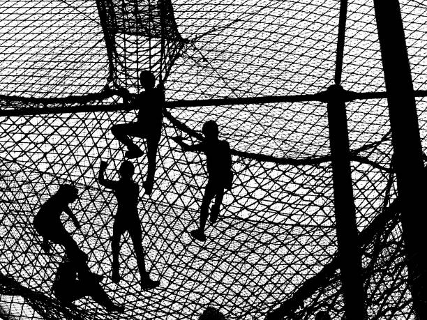 Black and white silhouette of a group of children climbing on a net. Net creates texture and pattern. Note: (Original is from film rather than digital.)