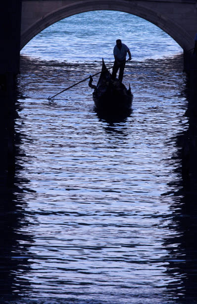 istock Gondolier Navigating Gondola Under Archway in Venice Canal 108128671