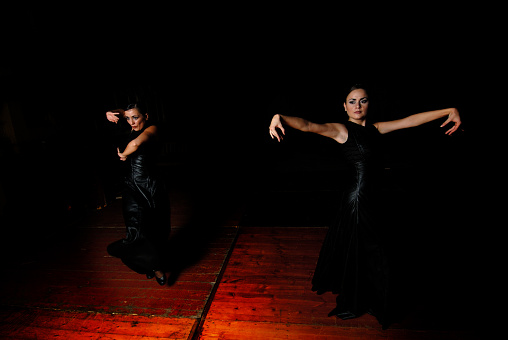 Dark image of flamenco dancers, with light focused on the dancer, black background.