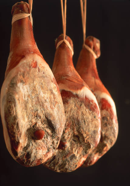 Three Pieces of Prosciutto Ham Hanging, Black Background stock photo