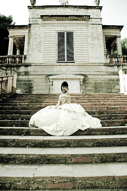 Young Princess dressed with evening gown sitting on stairs of ancient mansion.