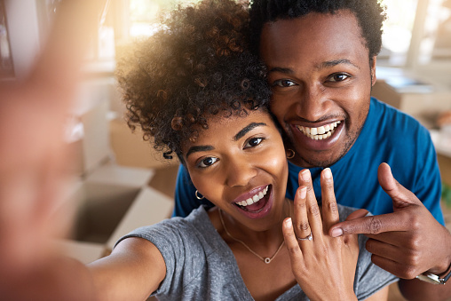 Cropped portrait of an affectionate young couple announcing their engagement with selfies while standing in their new home