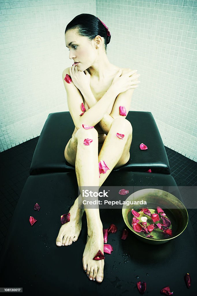 Jovem mulher sentada no Spa mesa com pétalas de rosas - Foto de stock de 20-24 Anos royalty-free