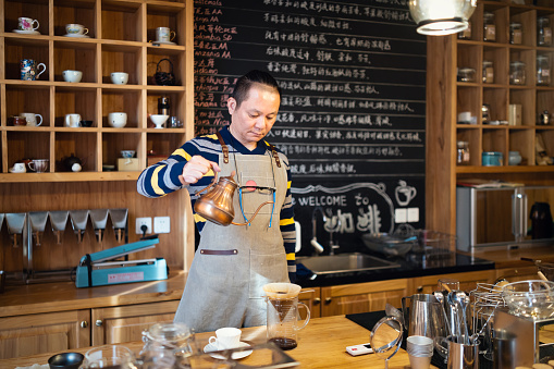 Male barista pouring hot water to make pour-over coffee.