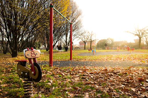 Red motorcycle spring rider in a park playground in autumn, with swings in the background and golden flare light on side. Background with copyspace.