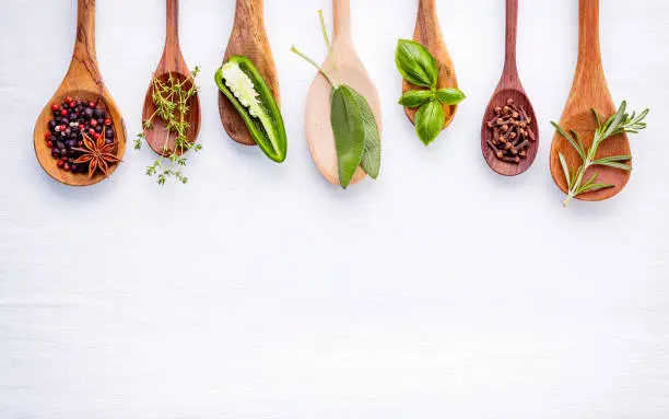 Photo of Various of spices and herbs on wooden background. Flat lay spices ingredients rosemary, thyme, oregano, sage leaves and sweet basil on white wooden.