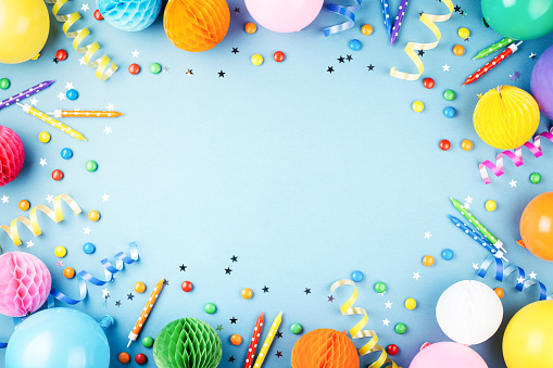 Birthday party background on blue. Top view. Frame made of colorful serpentine, balloons, candles, candies and confetti.