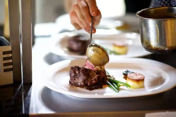 Photo of Steak on a plate being prepared in a Chef's kitchen sauce being poured