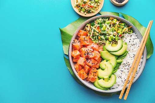 Tasty appetizing poke bowl served with salmon, avocado, rice, salad with edamame. Blue background. View from above. Horizontal.