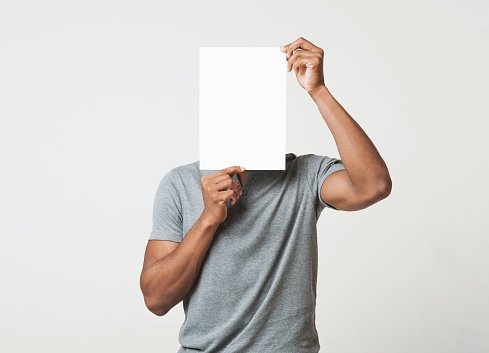African-american man covering his face with empty white paper like mask, try to hide his real emotion, copy space