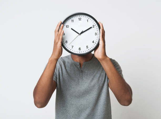 black man covering his face with big clock on white background - clock face fotos imagens e fotografias de stock