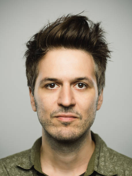 Real caucasian man with blank expression Close up portrait of young adult man with blank expression against gray background. Vertical shot of real caucasian man staring in studio with brown hair and modern haircut. Photography from a DSLR camera. Sharp focus on eyes. rockabilly hair men stock pictures, royalty-free photos & images