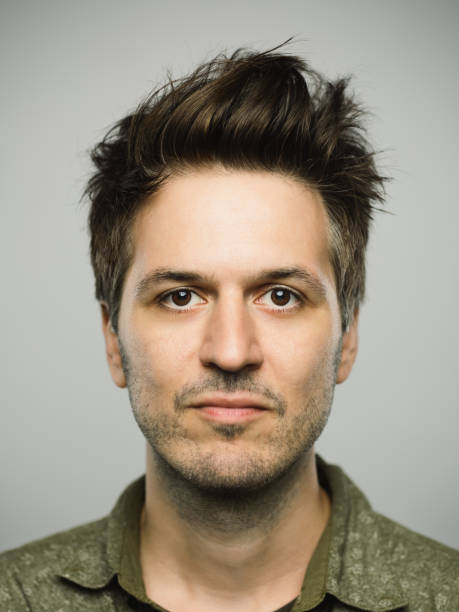 Real caucasian man with blank expression Close up portrait of young adult man with blank expression against gray background. Vertical shot of real caucasian man staring in studio with brown hair and modern haircut. Photography from a DSLR camera. Sharp focus on eyes. spiked hair stock pictures, royalty-free photos & images