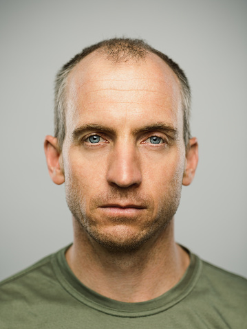 Close up portrait of mature adult adult caucasian man with blank expression against gray background. Vertical shot of real canadian man staring in studio with short balding hair and blue eyes. Photography from a DSLR camera. Sharp focus on eyes.