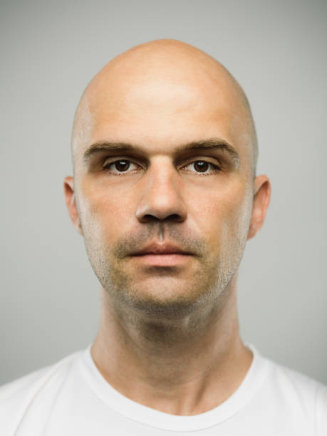 Real caucasian man with blank expression Close up portrait of mid adult adult caucasian man with blank expression against gray background. Vertical shot of real serbian man staring in studio with bald shaved head and brown eyes. Photography from a DSLR camera. Sharp focus on eyes. skin head stock pictures, royalty-free photos & images