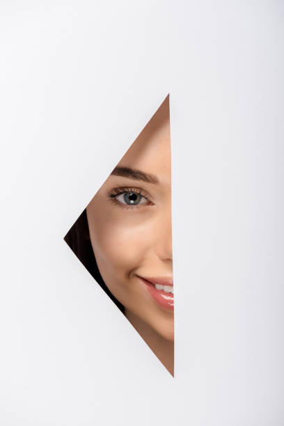 istock beautiful young woman smiling at camera through hole on white 1081396452