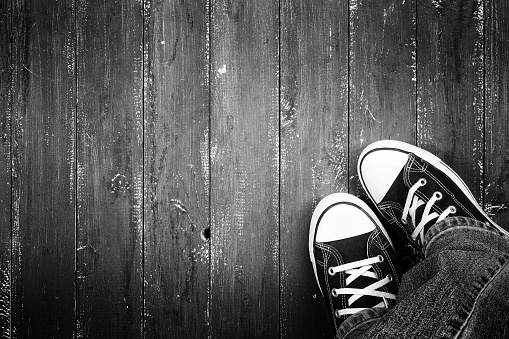 Clothes, shoes and accessories - Top view closeup legs put in gumshoes and jeans top view on a wooden background monochrome