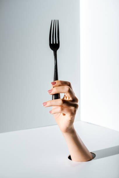 istock cropped image of woman holding fork in hand through hole on white 1081406608